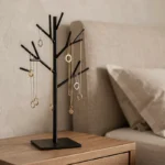Arbre à bijoux en métal noir avec colliers et bagues posé sur une table de chevet en bois dans une chambre élégante