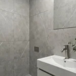 Salle de bain moderne avec dalle murale PVC finition béton mat gris, lavabo blanc et robinetterie en nickel brossé