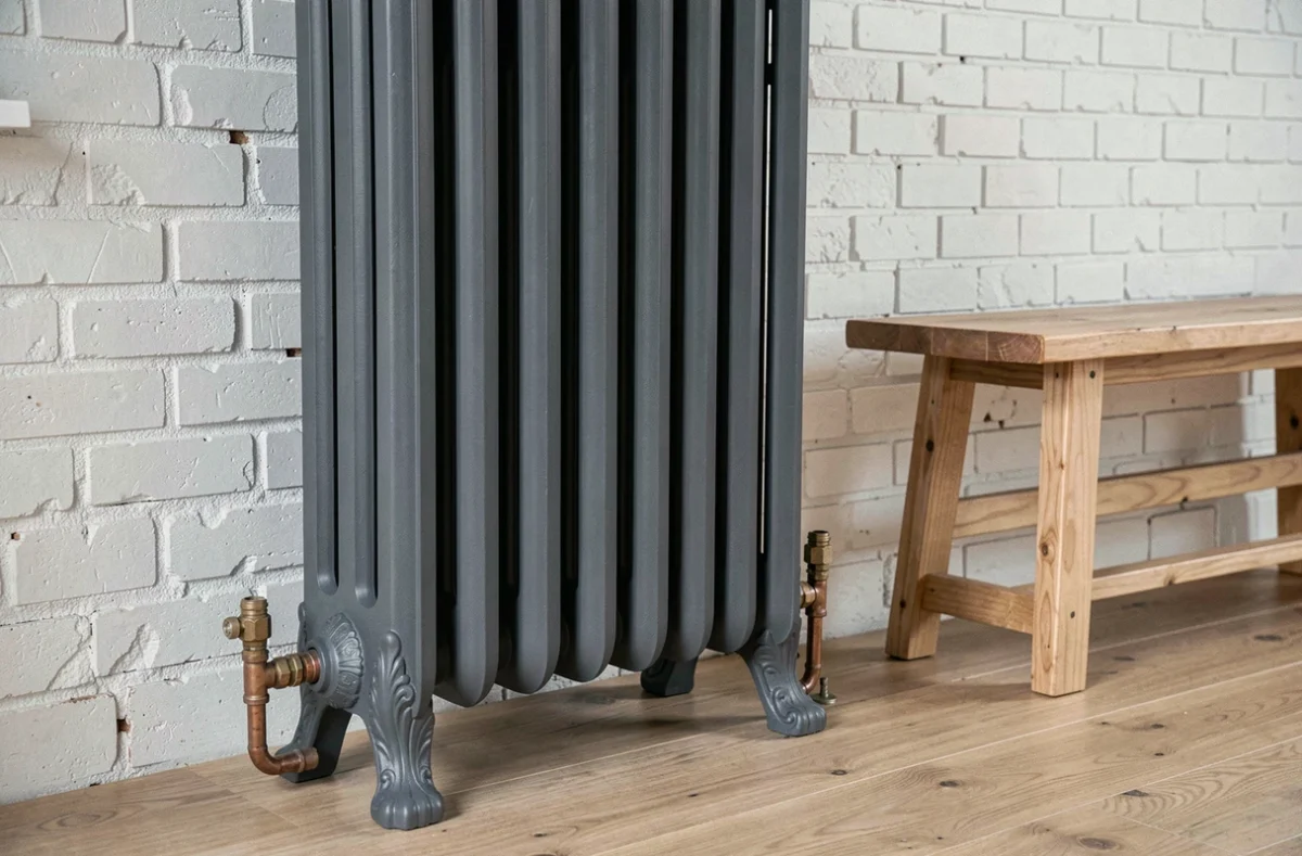 Radiateur en fonte entièrement rénové avec pied décoratif peint en gris anthracite dans un intérieur loft aux briques blanches