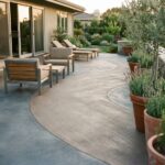 Terrasse moderne en béton décoratif texture balayée avec mobilier en acier brossé et plantes méditerranéennes