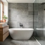 Salle de bain moderne rénovée en Haute-Garonne avec baignoire îlot, carrelage gris et robinetterie dorée